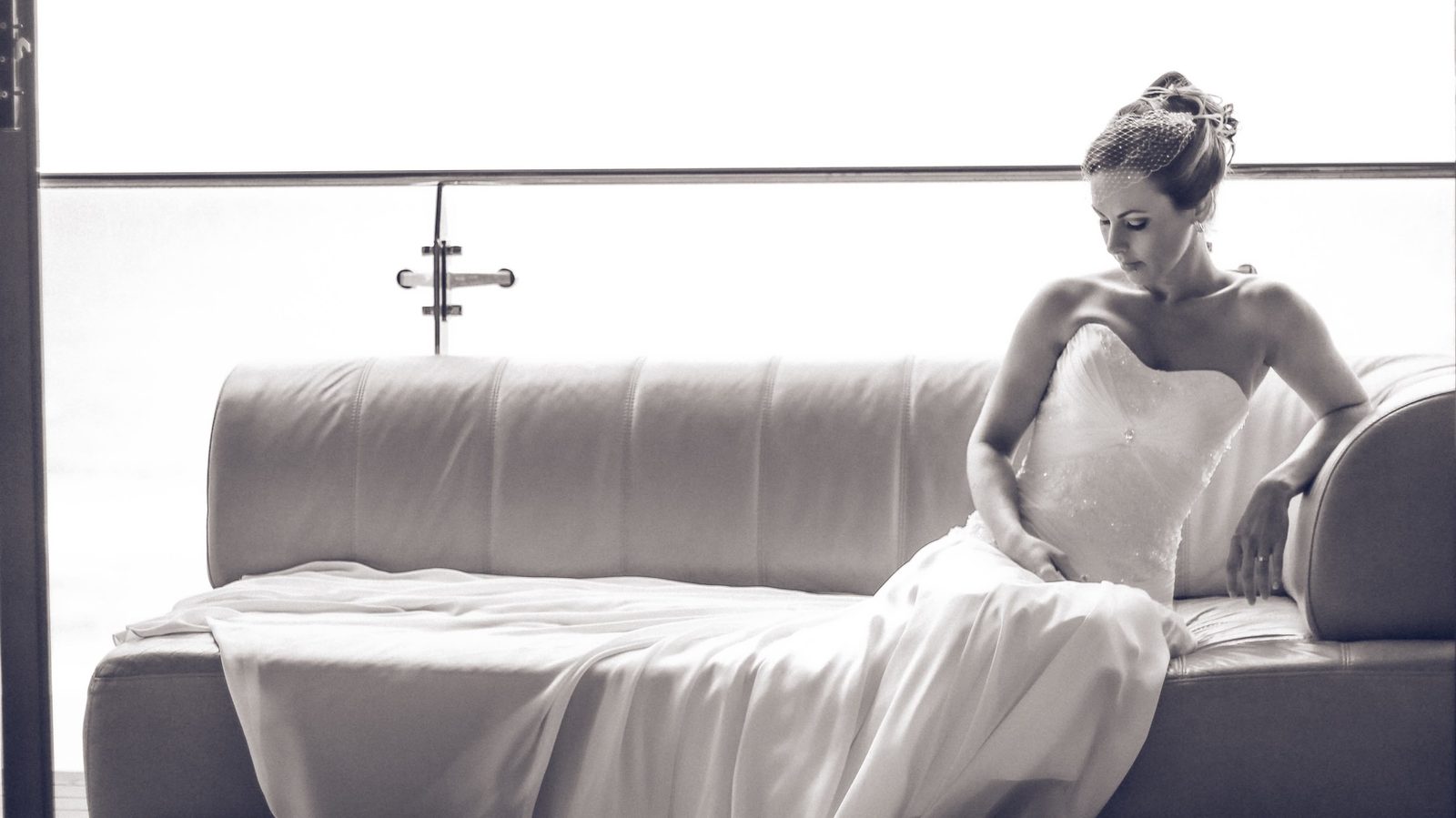 A bride seated in soft window light, her gown spread across a pale couch