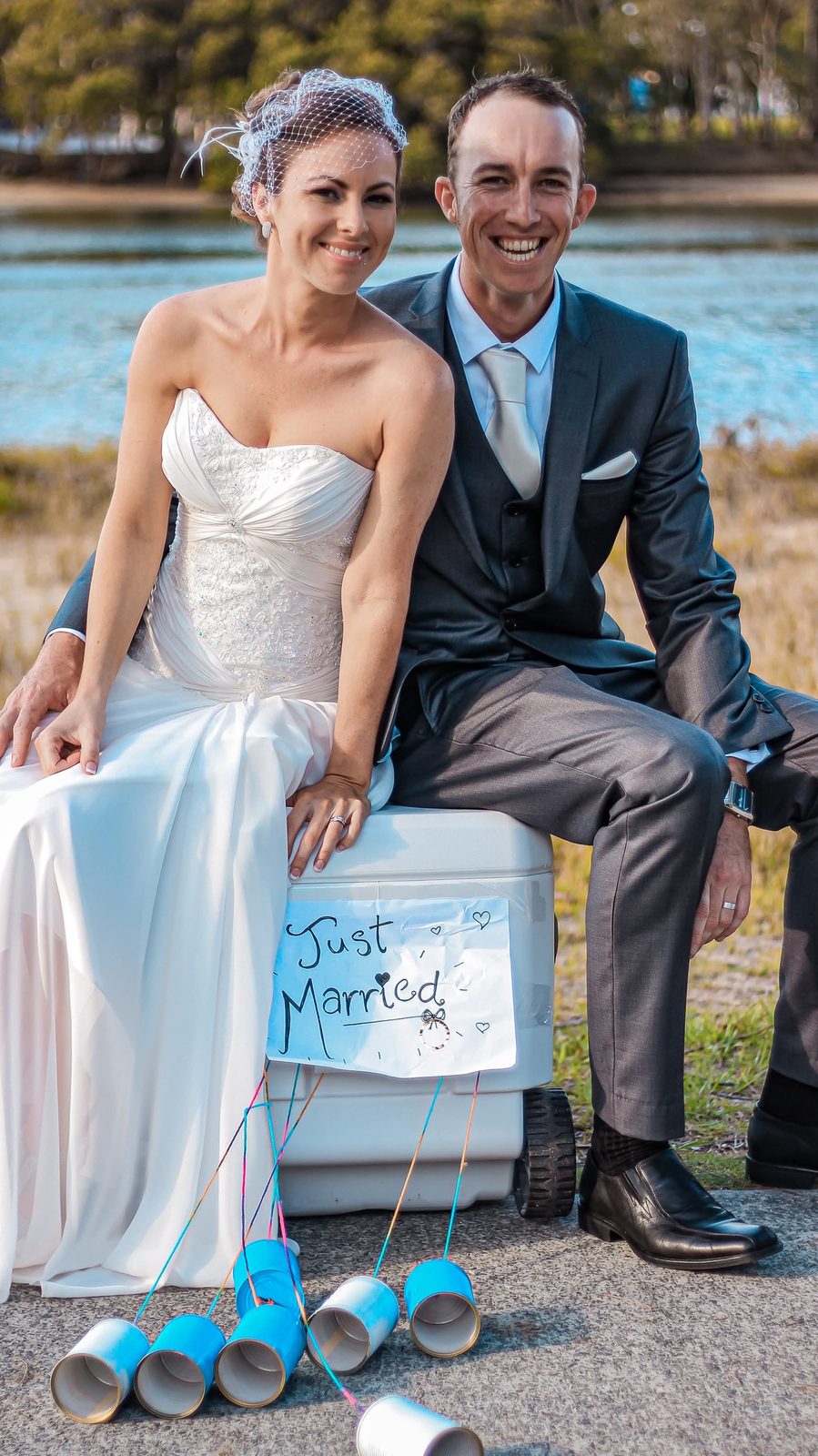A newly married couple sitting on an esky with a hand-written Just Married sign and tin cans
